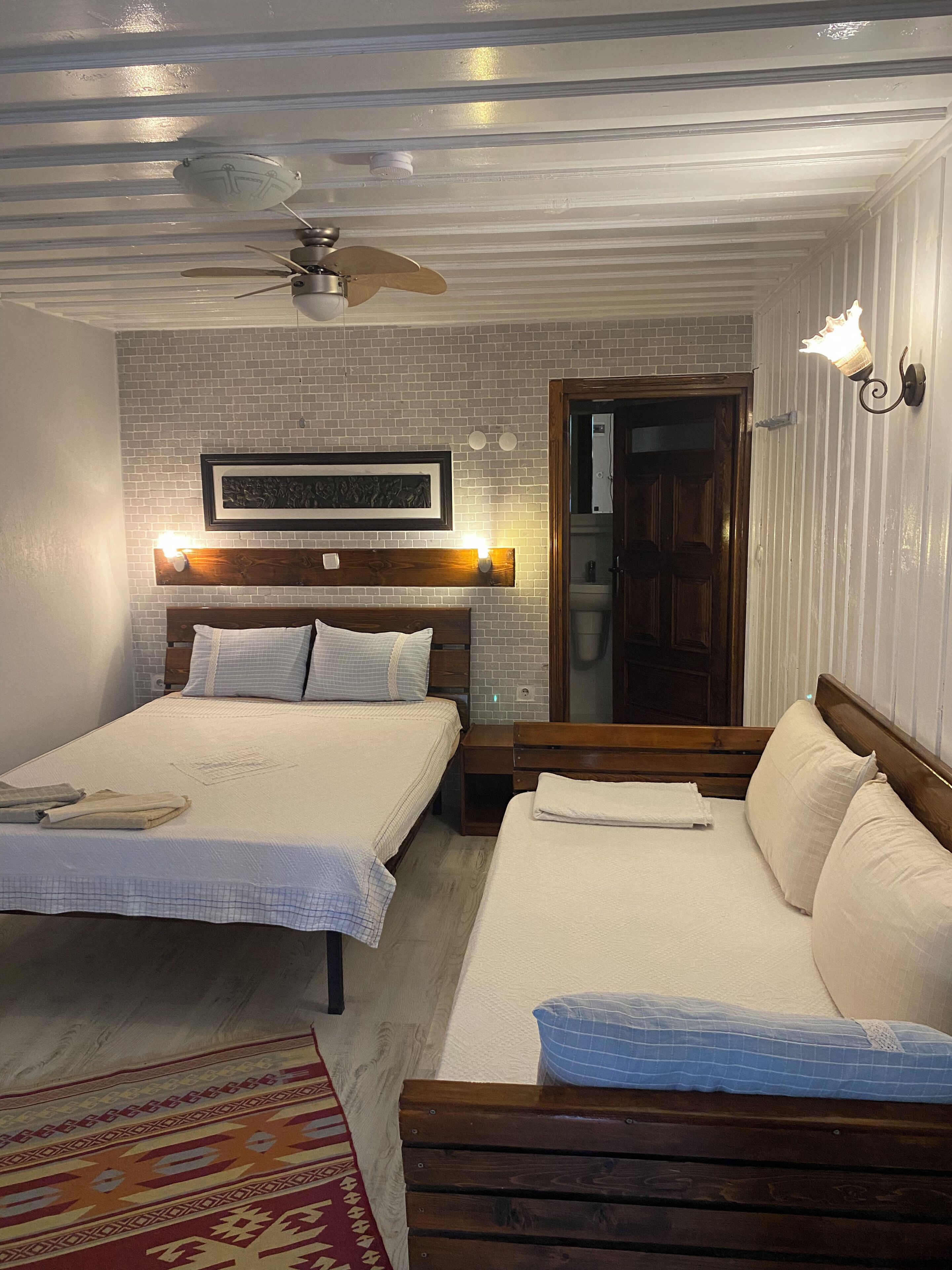 A hotel room with two beds, a ceiling fan, a wooden headboard, a framed artwork, and a nightstand with a lamp.