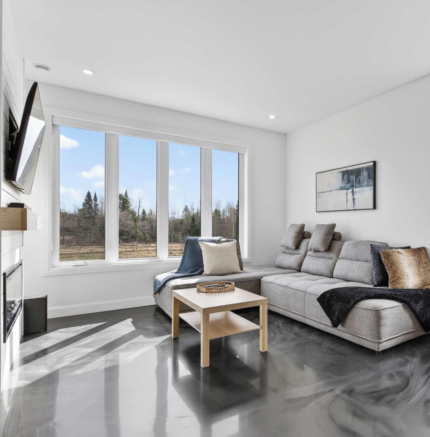 A modern living room with a sofa, coffee table, and a large window with a view of trees.