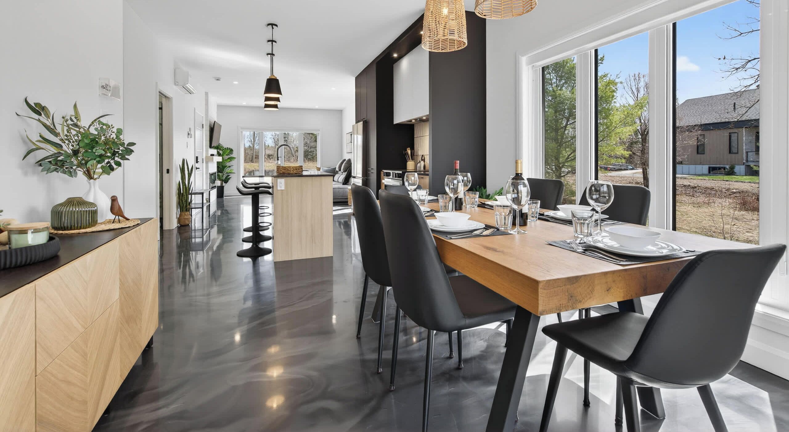 A modern kitchen with a dining area, large windows, and a view of the outdoors.