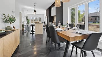 A modern kitchen with a dining area, large windows, and a view of the outdoors.