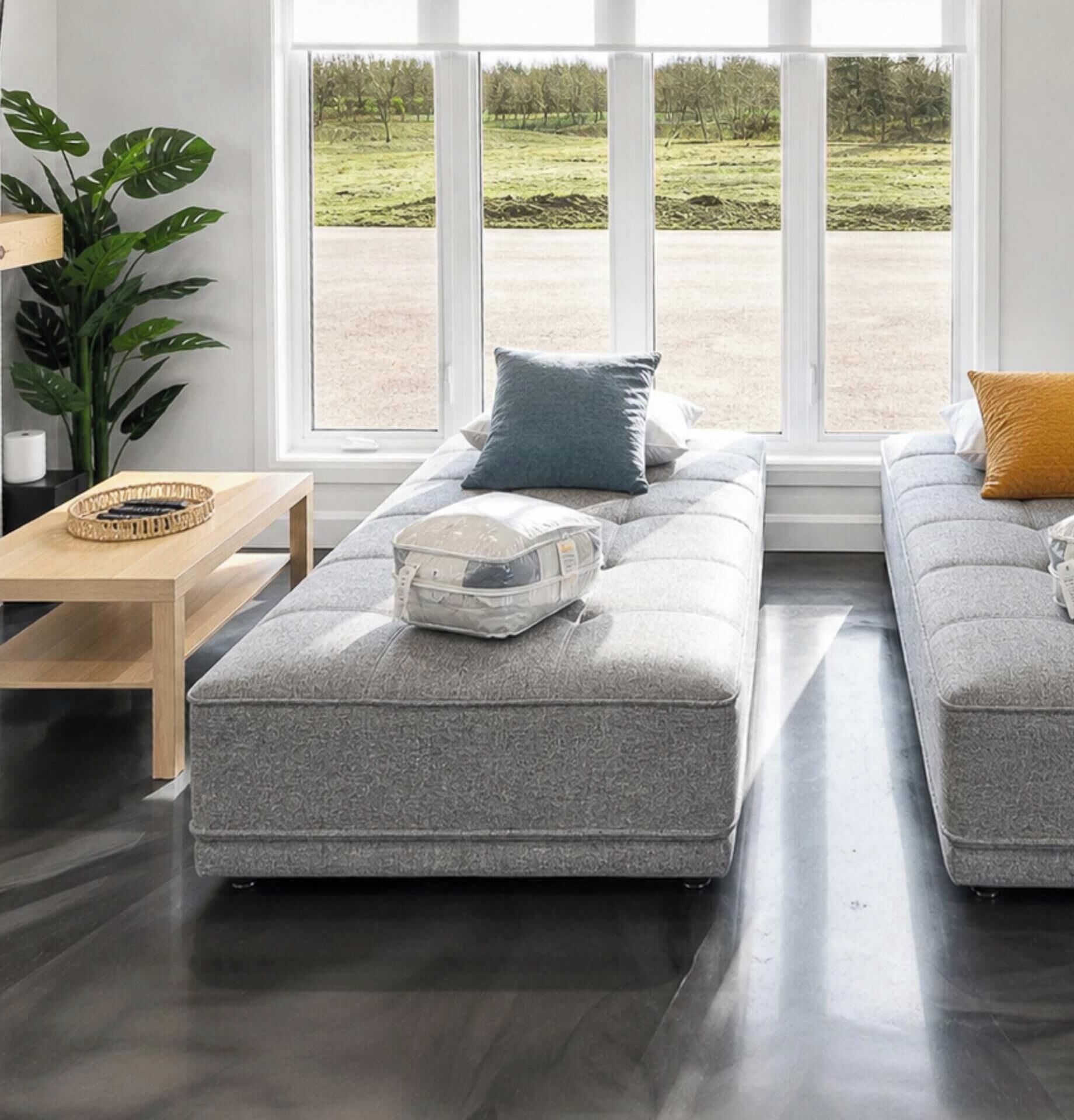 Una sala moderna con un sofá gris, una mesa de centro de madera y un amplio ventanal con vistas a un campo verde.