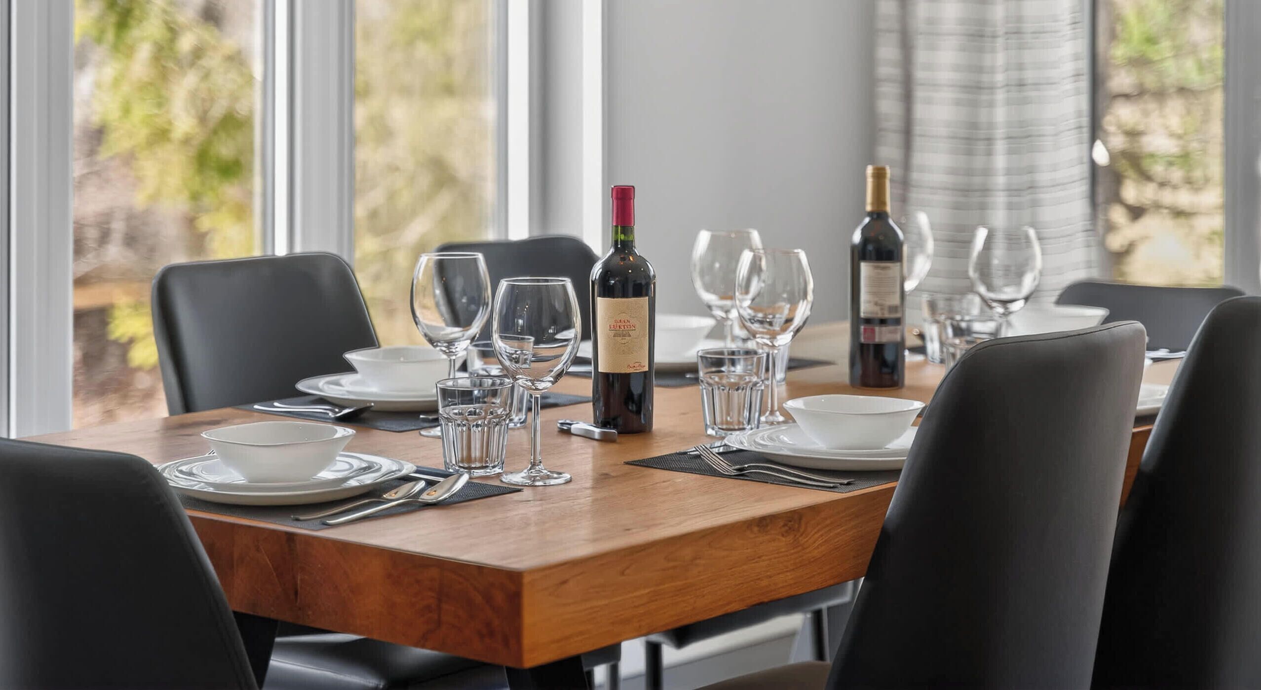 Een eettafel gedekt met wijnglazen, borden en bestek, met een fles wijn en een wijnglas op tafel.