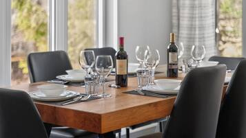 Een eettafel gedekt met wijnglazen, borden en bestek, met een fles wijn en een wijnglas op tafel.