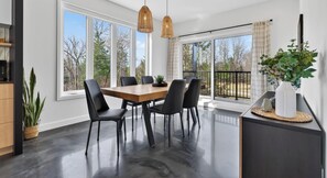 Un'area pranzo moderna con un tavolo in legno, sedie nere e un'ampia finestra con vista sugli alberi.