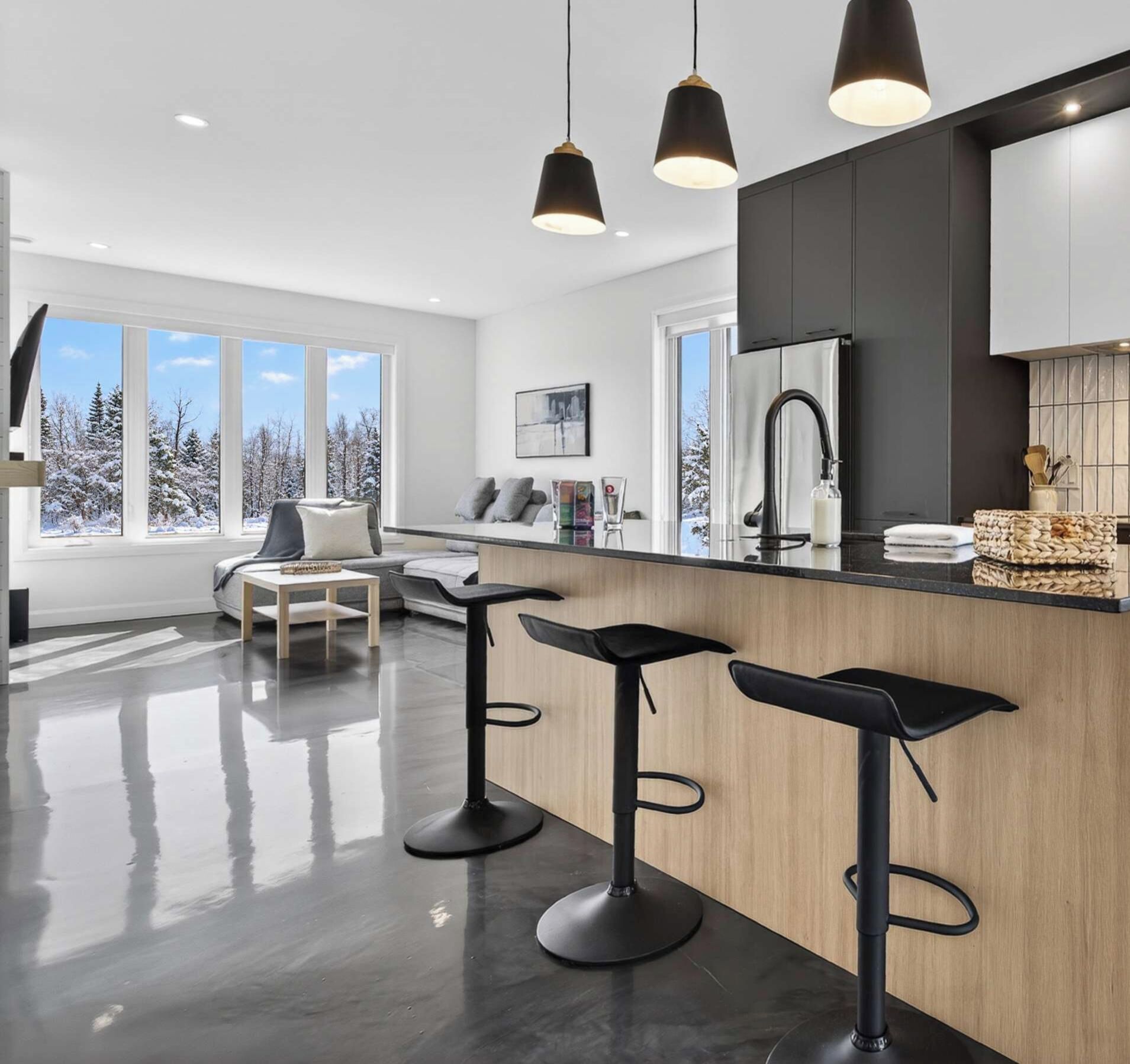 A modern kitchen with a bar area, large windows, and a view of a snowy landscape.