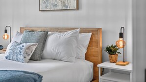 Un lit bien fait, avec une literie blanche et de nombreux oreillers, une tête de lit en bois et deux tables de chevet dotées de lampes au design moderne.