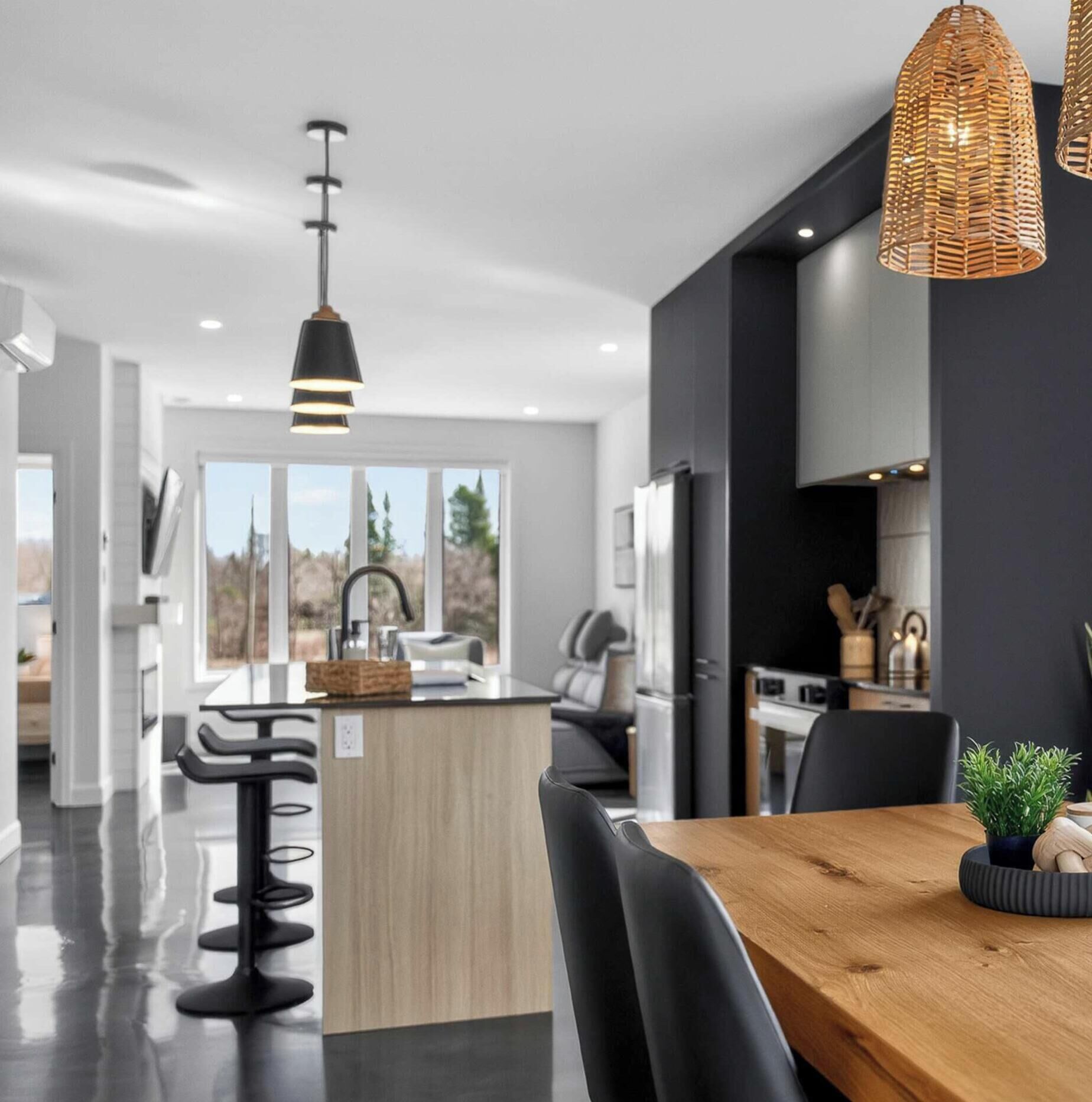 Une cuisine moderne dotée d’un îlot central, de tabourets de bar noirs et de luminaires suspendus.