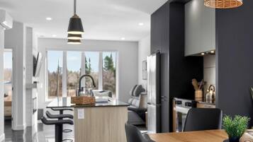 Une cuisine moderne dotée d’un îlot central, de tabourets de bar noirs et de luminaires suspendus.