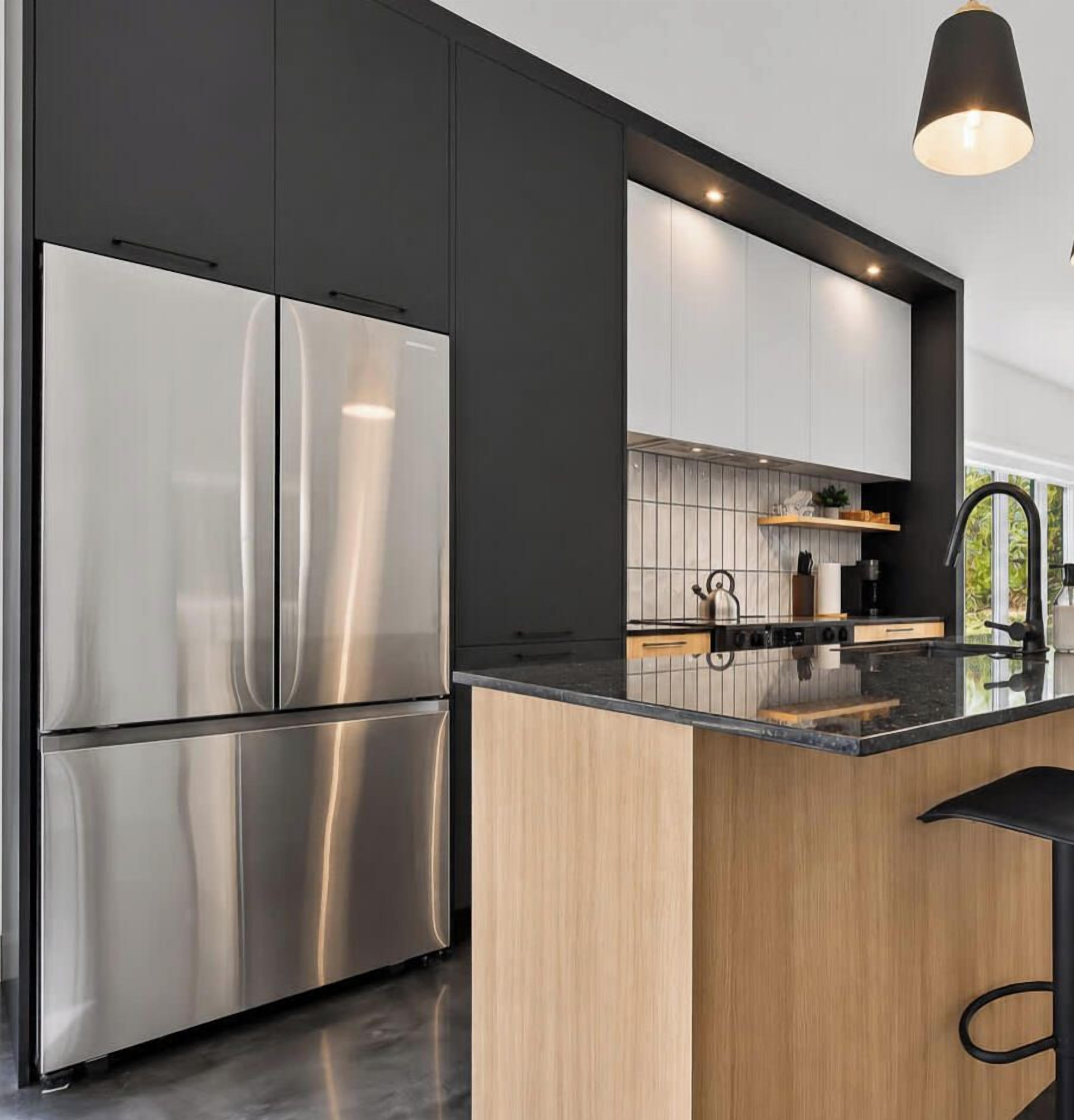 A modern kitchen with stainless steel appliances, wooden cabinetry, and a black countertop.