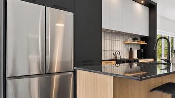 A modern kitchen with stainless steel appliances, wooden cabinetry, and a black countertop.