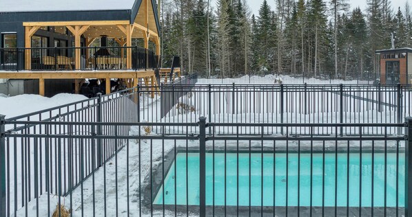 A pool surrounded by a metal fence, with a building featuring a wooden deck and chairs in the background. - Le Sofia - Spa, Mezzanine Pool Table, Luxury 12p (Shannon)