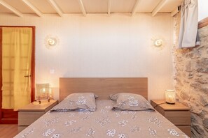 A bedroom with a wooden headboard, two bedside tables with lamps, a bed with floral bedding, and a stone wall.