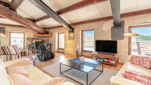 A spacious living room with a sofa, a coffee table, a TV, and a view of the outdoors. - Apartment “Maison d’Odette” with Lagoon View, Wi-Fi, and Air Conditioning (Gruissan)
