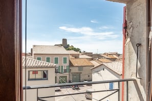 A view from a window overlooking a street with buildings, a tower, and parked cars.