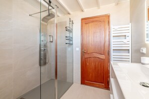 Une salle de bain avec une douche Ă parois de verre, une porte en bois et un lavabo blanc.
