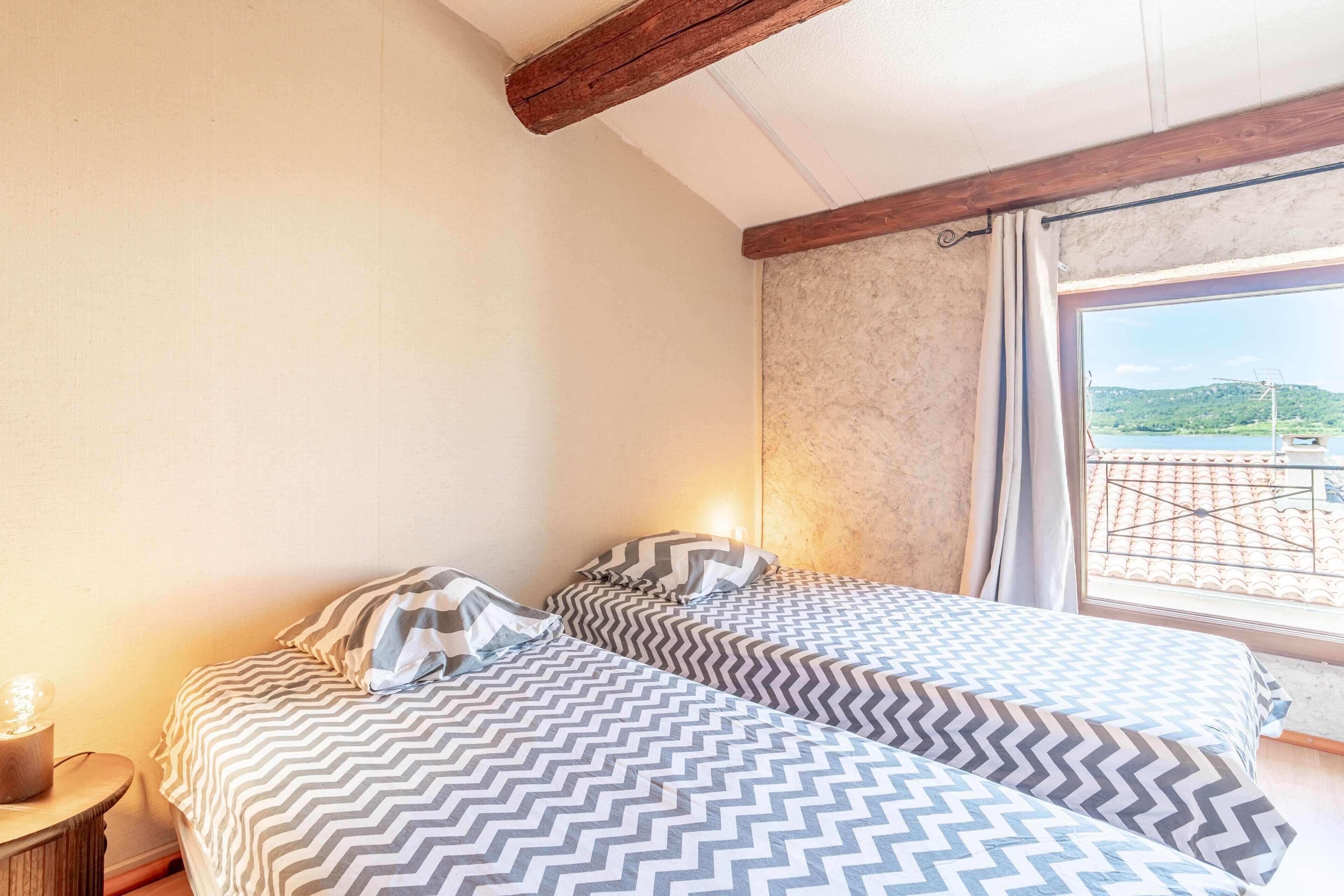 A bedroom with two beds, a wooden headboard, a window with a view, and a bedside lamp.