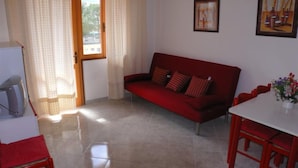 Una sala de estar con un sofá rojo, una mesa blanca y sillas, un televisor y dos cuadros en la pared.