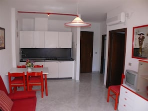 Eine moderne Küche mit weißen Schränken, einem Esstisch mit roten Stühlen und einer TV-Konsole mit Fernseher.