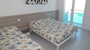 Een kamer met twee bedden, een houten hoofdbord, een kunstwerk aan de muur en een schuifdeur van glas die leidt naar een buitenruimte.