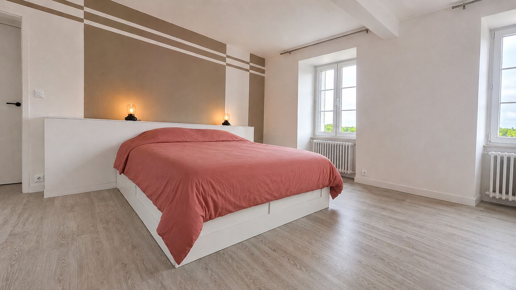 Un dormitorio con cama, cabecera blanca, radiador y ventana.