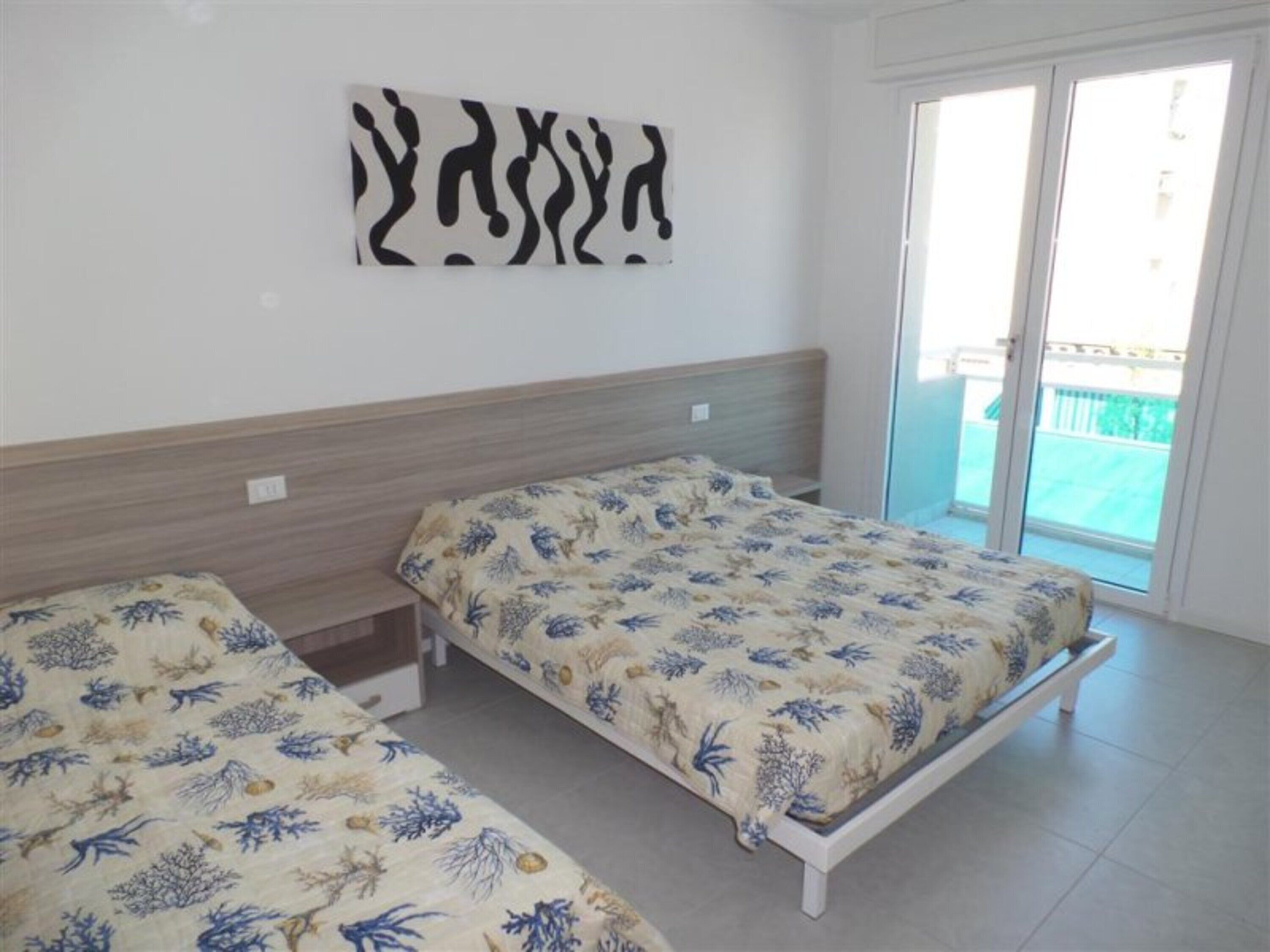 A room with two beds, a wooden headboard, a wall art piece, and a sliding glass door leading to an outdoor area.