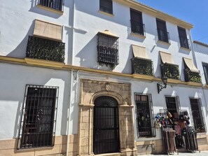 A white building with multiple balconies, a central arched doorway, and a small shop with items displayed outside. - Tradicional Casa amplia y luminosa con una ubicación excepcional en Ronda (Ronda)