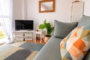 Ein Wohnzimmer mit Fernseher, Sofa, Pflanze und einem Kissen mit Muster.