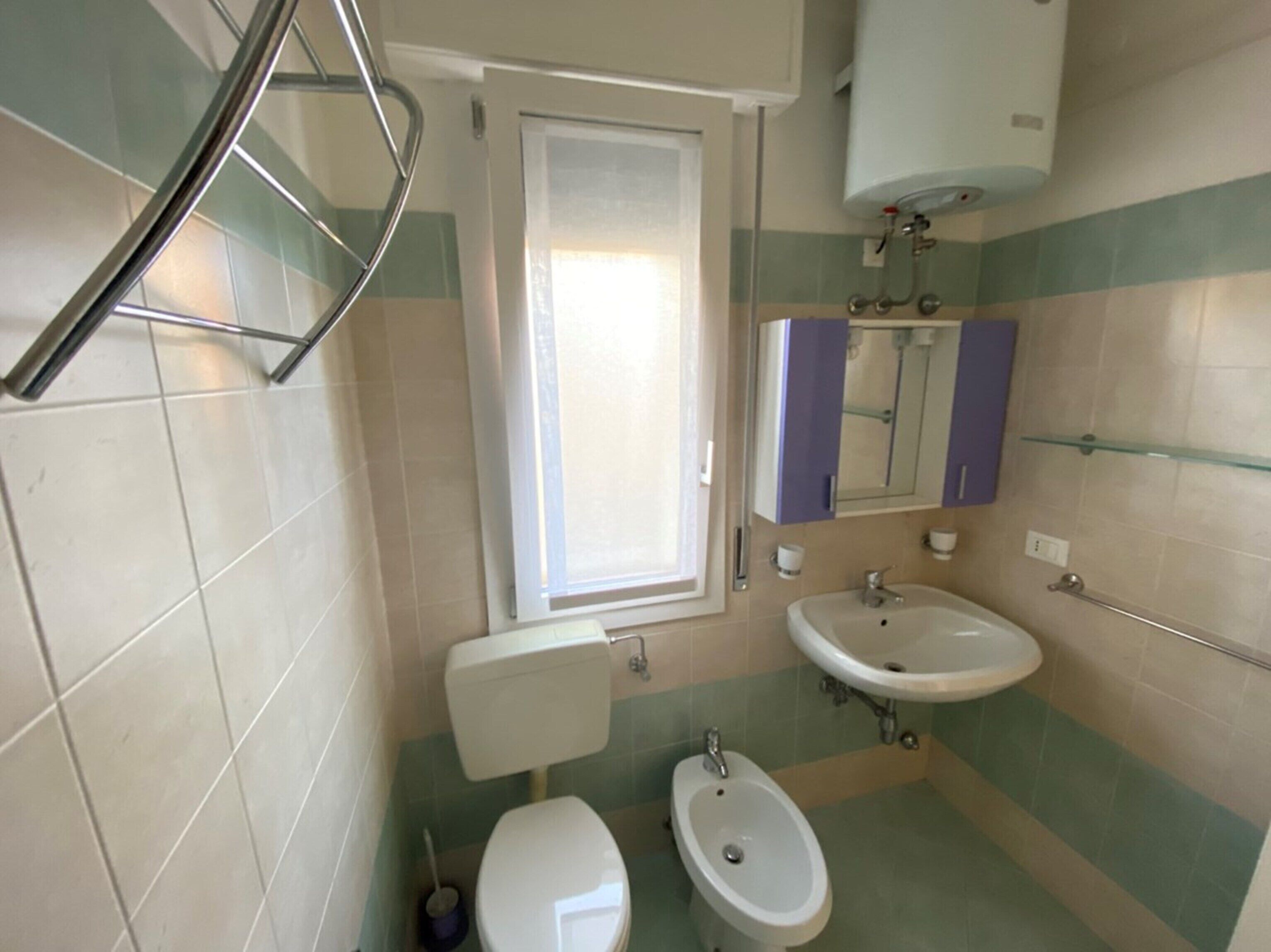 A bathroom with a toilet, bidet, sink, and a window.