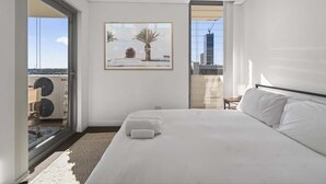 Habitación de hotel con una cama grande, un cuadro, una puerta corrediza de vidrio a un balcón y vistas de la ciudad.