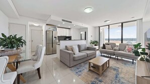 Una sala de estar moderna con sofá, mesa de centro y sillones, un área de cocina y ventanas grandes que ofrecen vistas.