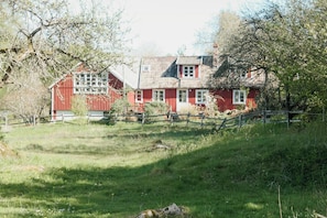 A red wooden house with a fenced yard, surrounded by trees. - 1909 farmhouse cottage (Vinslöv)