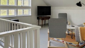 A room with a sloped ceiling, a television on a wooden stand, a desk, a chair, and a crib. - 1909 farmhouse cottage (Vinslöv)
