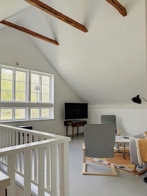 A room with a sloped ceiling, a television on a wooden stand, a desk, a chair, and a crib. - 1909 farmhouse cottage (Vinslöv)