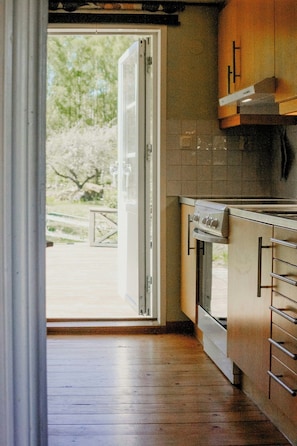 A kitchen with a stove, oven, and cabinets, leading to a glass door opening to a patio area. - 1909 farmhouse cottage (Vinslöv)