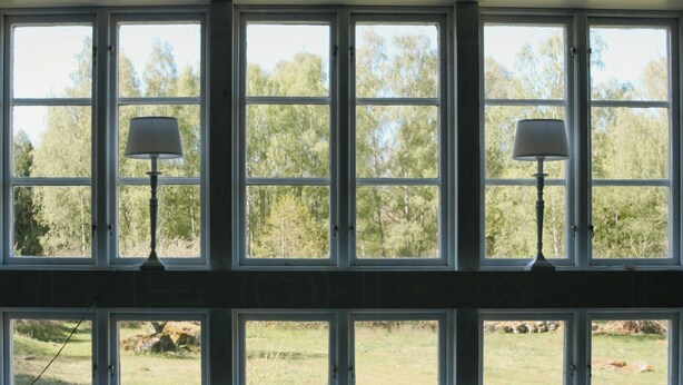 A room with multiple windows, each with a lamp. The windows provide a view of a grassy outdoor area with trees. - 1909 farmhouse cottage (Vinslöv)