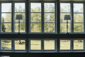 A room with multiple windows, each with a lamp. The windows provide a view of a grassy outdoor area with trees. - 1909 farmhouse cottage (Vinslöv)