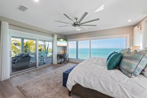 A bedroom with a large bed, a ceiling fan, a view of the ocean, and a sliding glass door leading to a balcony. - Beachfront Bliss by Beach Boutique Rentals (Anna Maria)