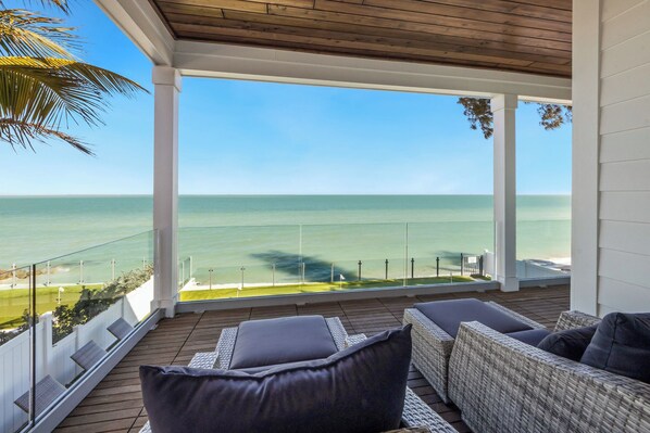 A covered balcony with wicker furniture and a view of the ocean. - Beachfront Bliss by Beach Boutique Rentals (Anna Maria)