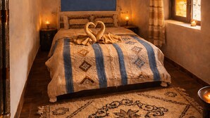 Une chambre à coucher avec un lit, un luminaire suspendu, une fenêtre avec des rideaux et un tapis à motifs.