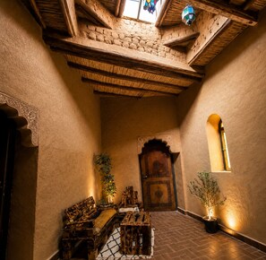 Un interior tradicional con un banco de madera, una puerta con intrincados grabados y una ventana pequeña.