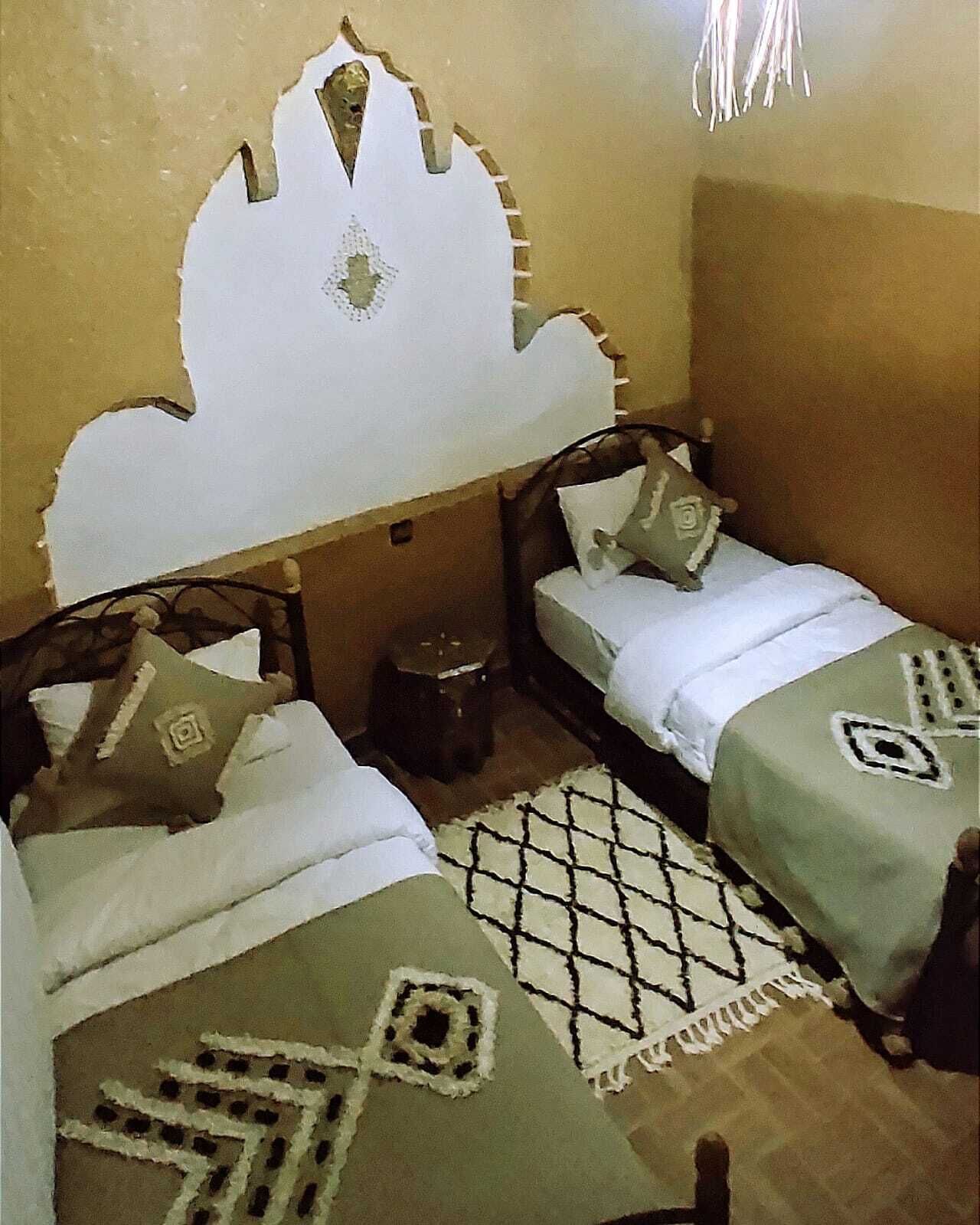 Ein Zimmer mit zwei Betten, einem gemusterten Teppich und einem dekorativen Wandvorhang.