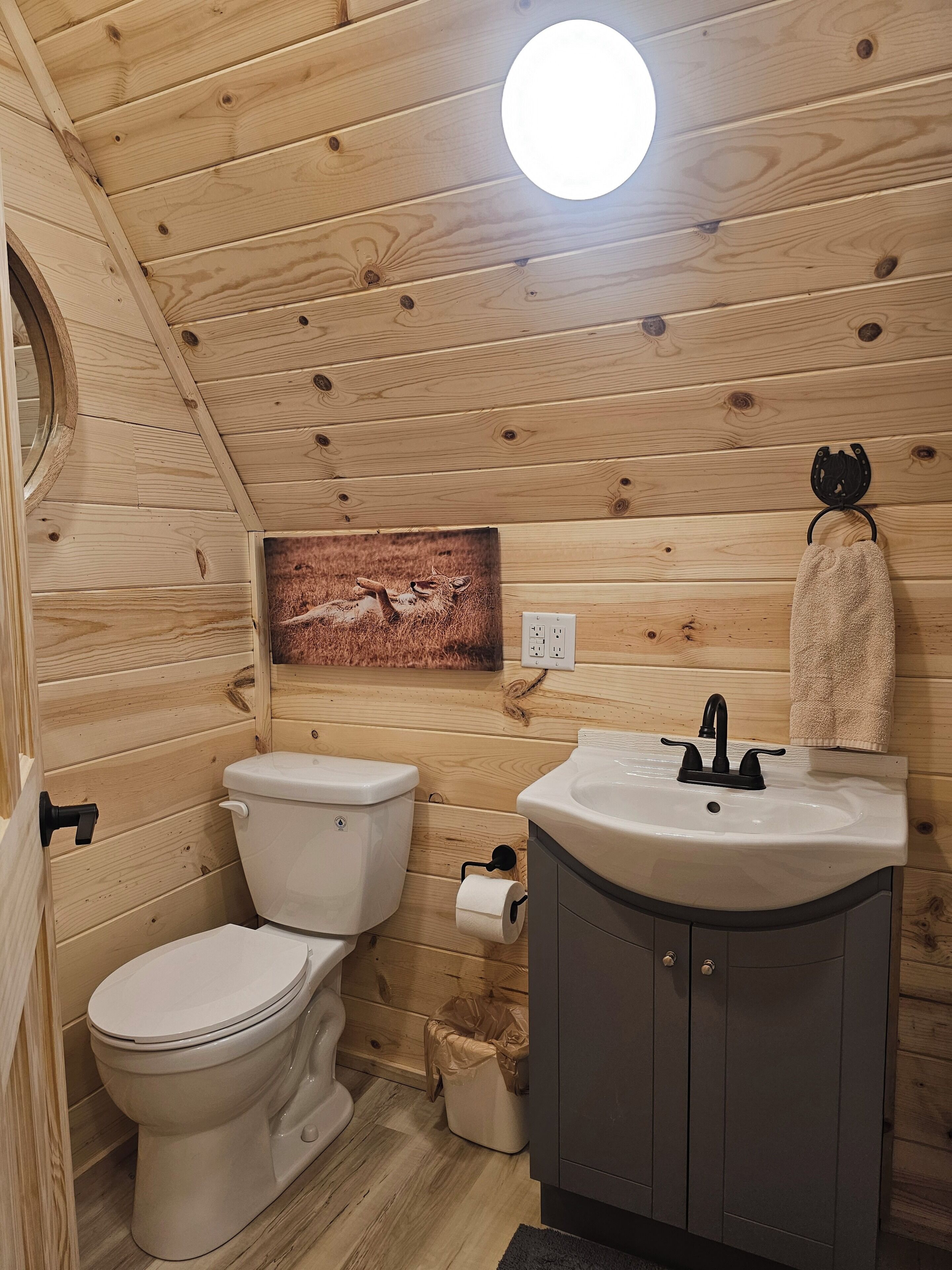 Een betegelde badkamer met toilet, wastafel en een rond raam.
