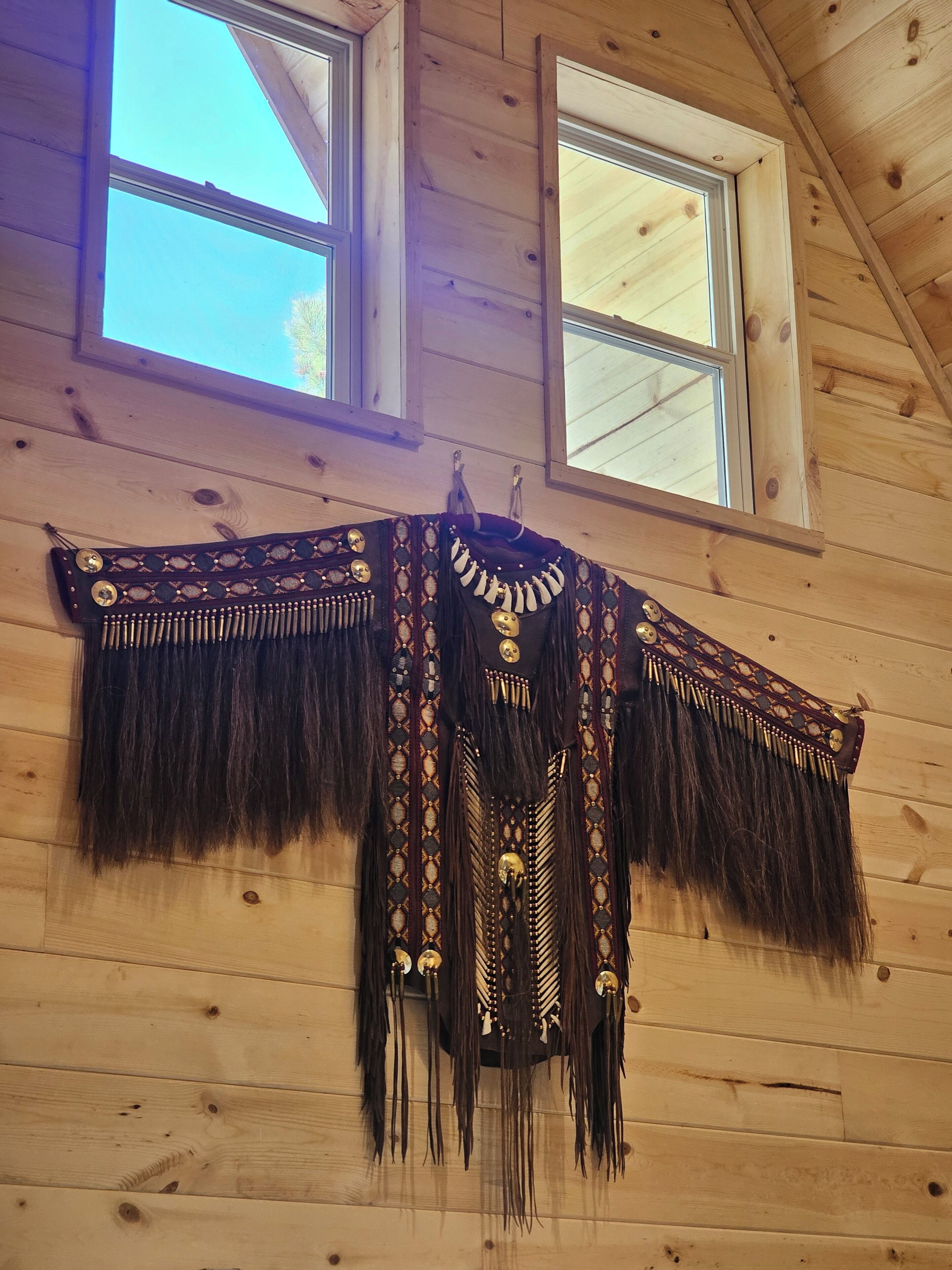 Un intérieur en bois avec deux fenêtres et un vêtement orné d’une frange décorative accroché au mur.