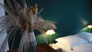 Una habitación con una cama, una mesita de noche, una lámpara y un florero con plantas secas.