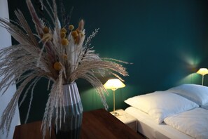 Ein Zimmer mit einem Bett, einem Nachttisch, einer Lampe und einer Vase mit Trockenblumen.
