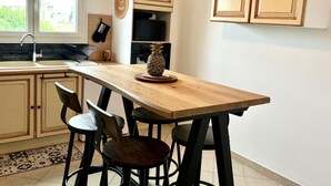 A kitchen with a wooden island, two black bar stools, a pineapple decoration, and a plant on the wall. - Seafront Palatino Apartment for 8 (Martigues)
