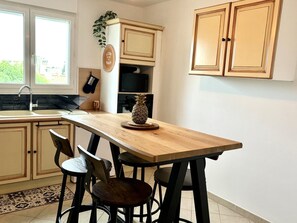 A kitchen with a wooden island, two black bar stools, a pineapple decoration, and a plant on the wall. - Seafront Palatino Apartment for 8 (Martigues)