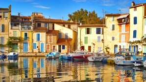 A waterfront with boats docked, buildings with balconies, and a clear sky. - Seafront Palatino Apartment for 8 (Martigues)
