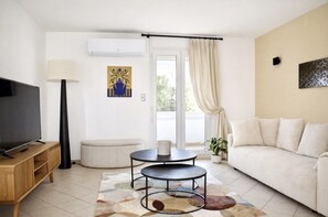 A living room with a TV, sofa, two tables, a lamp, and a potted plant. - Seafront Palatino Apartment for 8 (Martigues)