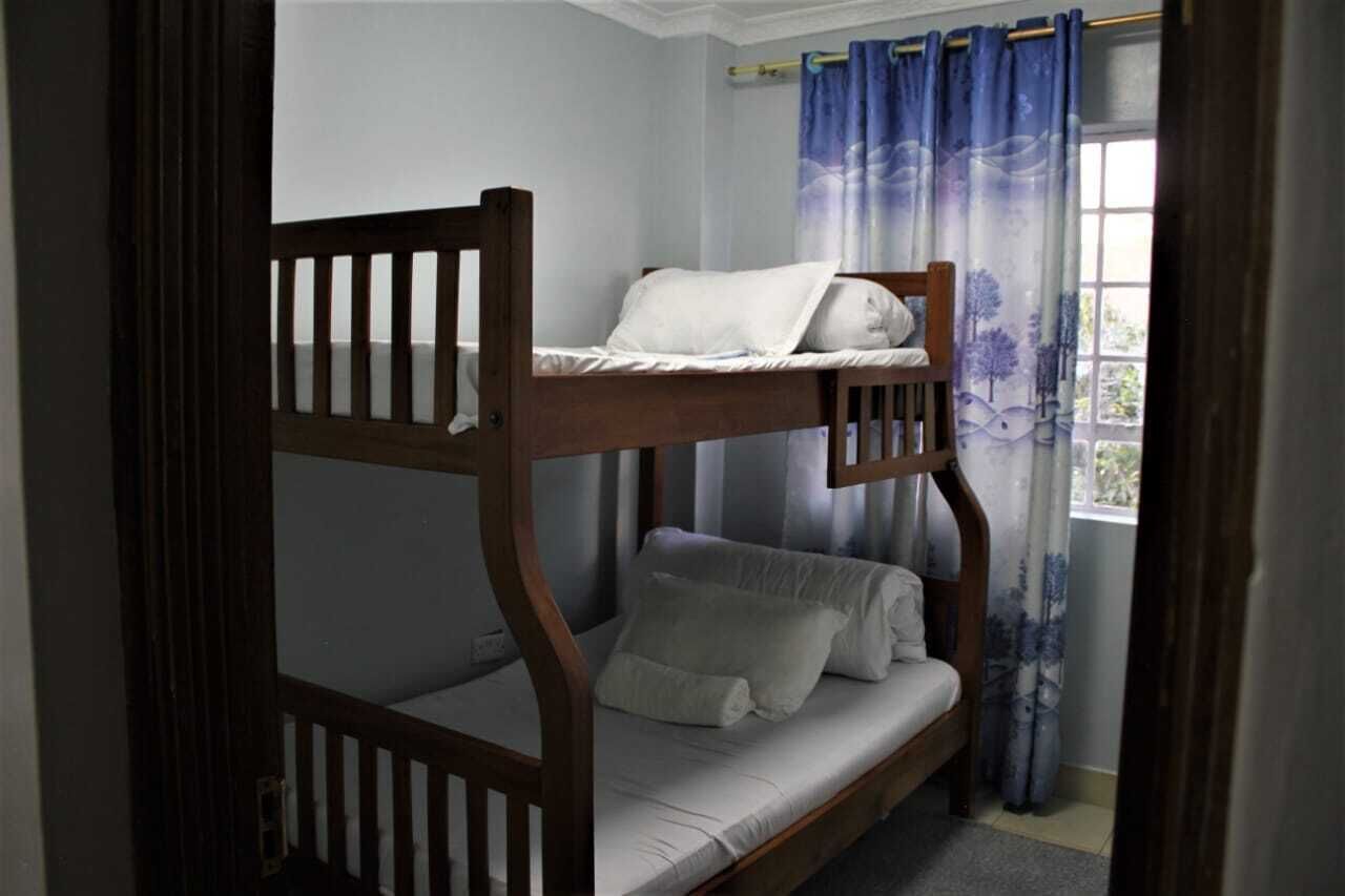 A bunk bed with a lower bunk, a window with blue curtains, and a view of greenery outside.